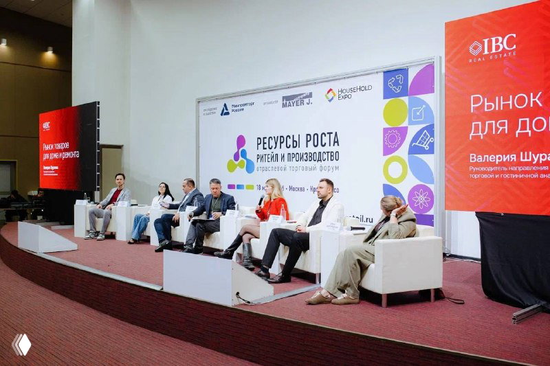 Панельная сессия на форуме: модератор и эксперты на сцене, видны экран и стенд IBC Real Estate с названием сессии