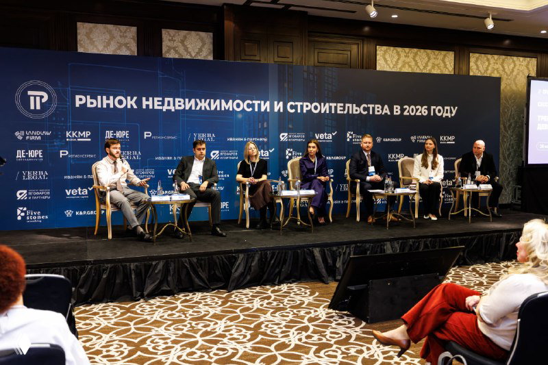 Панельная дискуссия на конференции «Рынок недвижимости и строительства в 2026 году»: эксперты сидят на сцене перед баннером мероприятия.