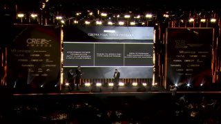 Фотография сцены CRE Awards 2026 с ведущим перед большим экраном и залом — кадр с церемонии награждения IBC Real Estate.