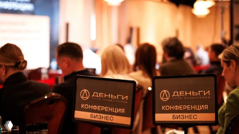 Зал конференции «Деньги»: участники в зале, фокус на табличках с логотипом «Деньги», деловая публика на мероприятии по коммерческой недвижимости