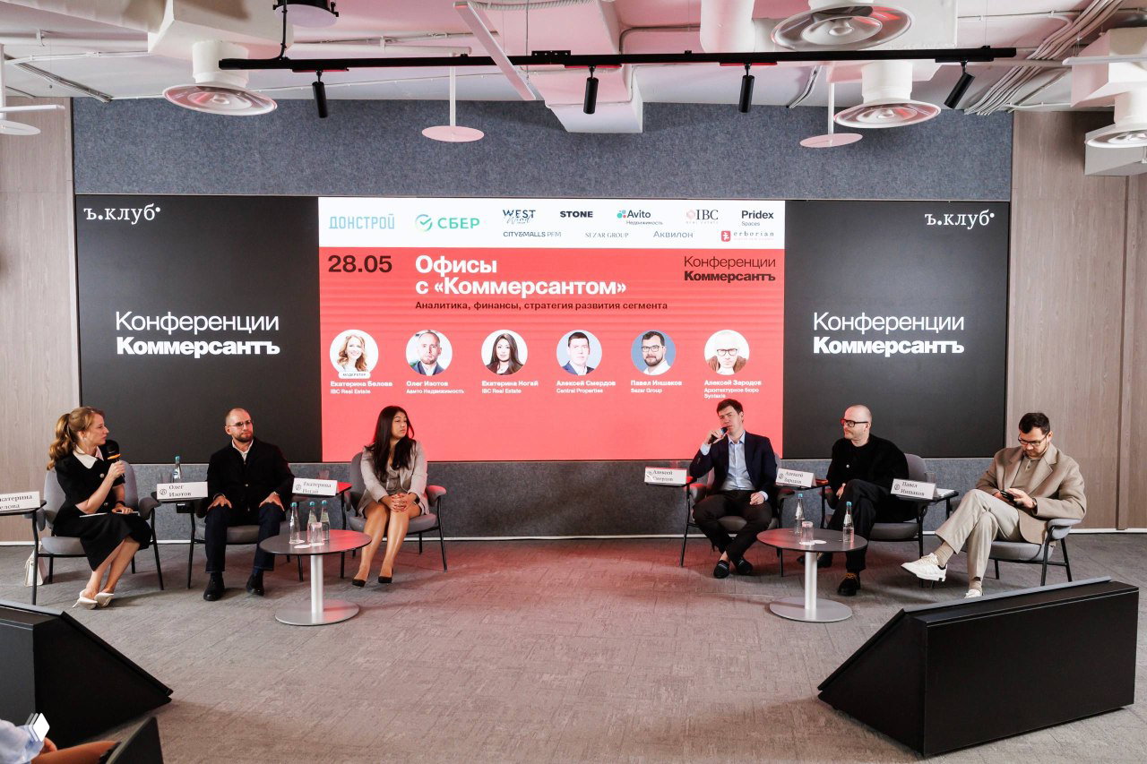Широкий план сцены конференции «Офисы с Коммерсантом»: панель экспертов на фоне большого экрана с программой и логотипами спонсоров.
