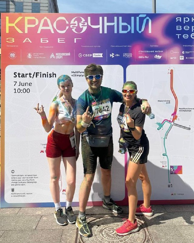 Трое участников IBC в спортивной форме позируют перед баннером «Красочный забег», видна карта трассы, дата и логотип мероприятия.