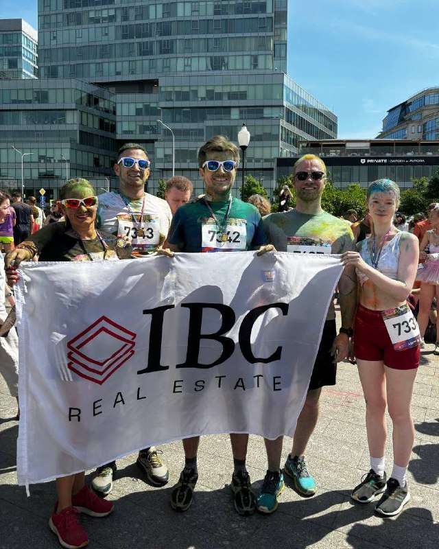 Команда IBC держит баннер компании на городской площади: пятеро сотрудников в разноцветной пудре позируют на финише после забега.