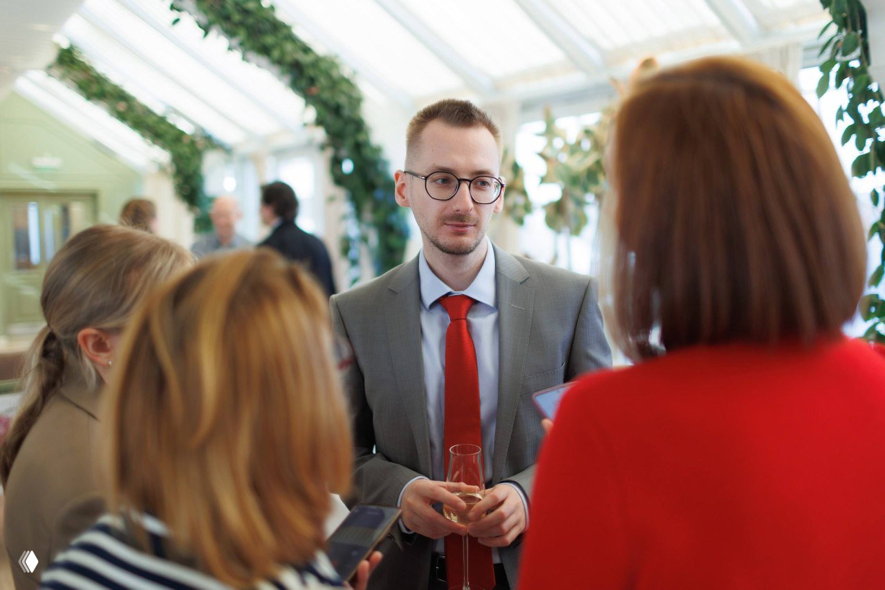 Представитель IBC Real Estate в сером костюме и красном галстуке общается с журналистами и гостями во время фуршета пресс‑завтрака.