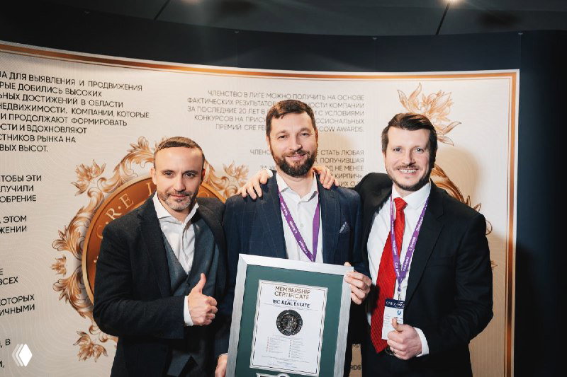 Трое сотрудников IBC Real Estate держат сертификат почётного члена CRE League на фоне бренд-стены мероприятия CRE X-mas.