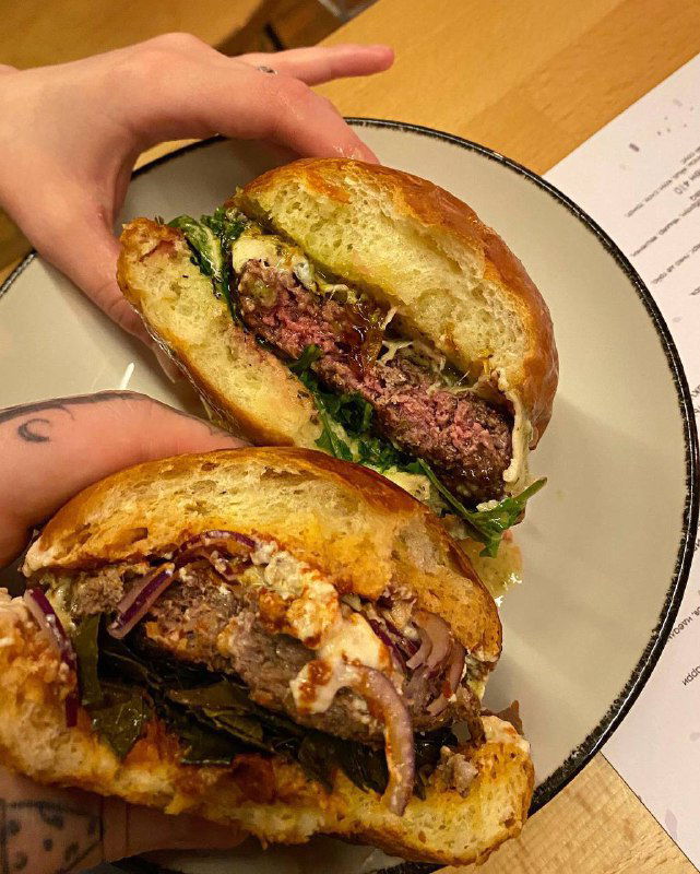 Разрезанный бургер в руке: видна идеальная прожарка котлеты, салат и соусы на булочке — крупный план, демонстрация начинки перед едой.