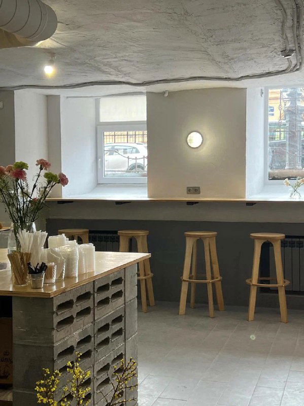 Минималистичный светлый интерьер с барной стойкой, табуретами и вазой с цветами — место для быстрого кофе и разговоров.