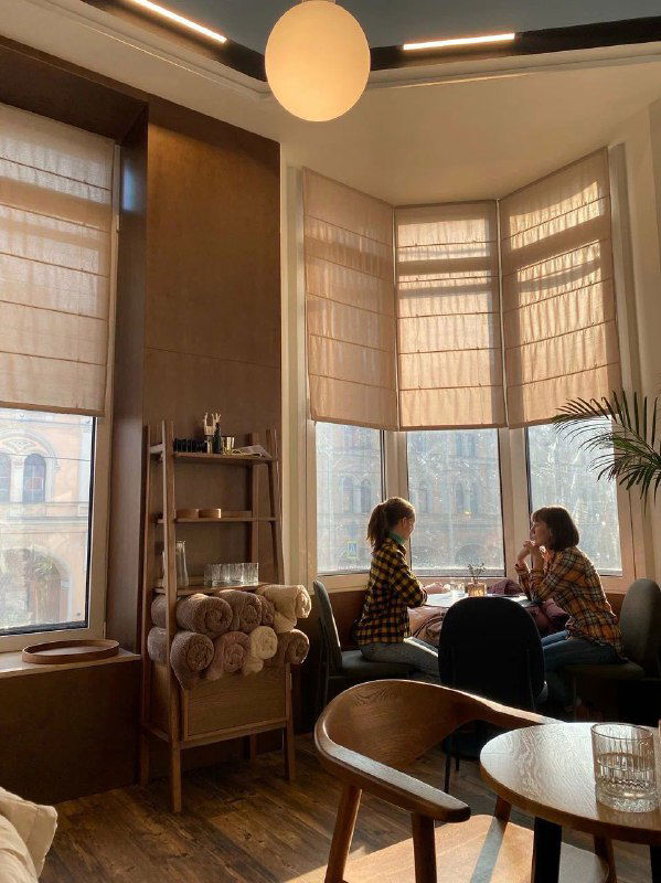 Зал кафе с большими эркерами, римскими шторами и комфортными креслами — светлое пространство для встреч и неспешного кофе.