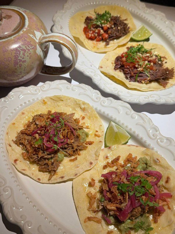 Три тако на белой тарелке: томлёная говядина и утка, лайм, маринованный лук и зелень — крупный план, видно текстуру начинки и лепёшек.