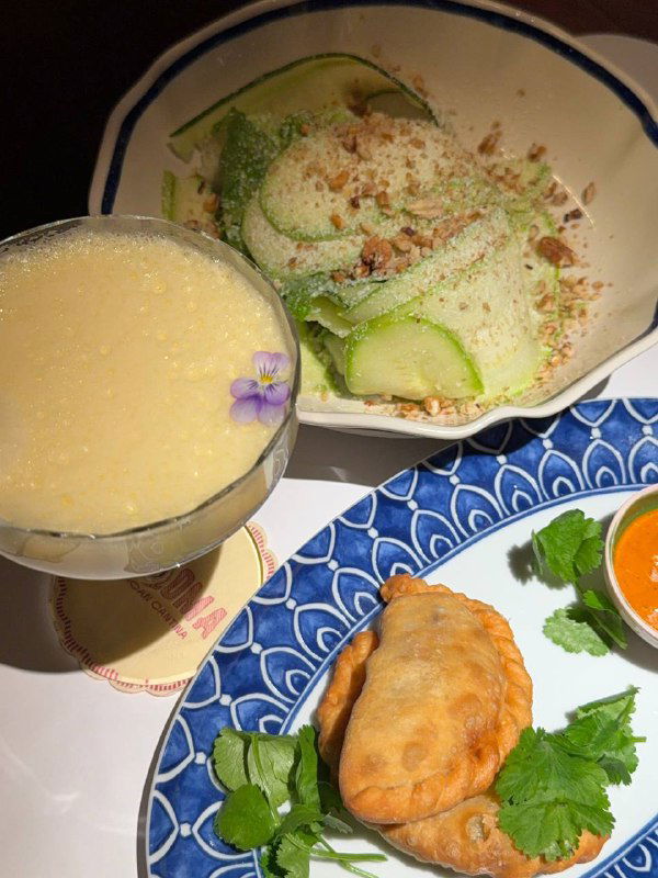 Тарелка с зелёным салатом и эмпанадас: свежие листья, тонкие ломтики огурца, золотистые пирожки с обильной начинкой и мисочка с сальсой рохо.