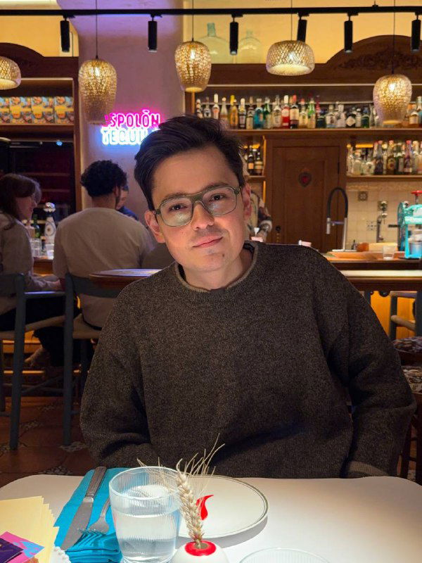 Гость за столом в Paloma Cantina: молодой человек в очках на фоне бара, перед ним тарелка и бокал, тёплая и уютная атмосфера заведения.