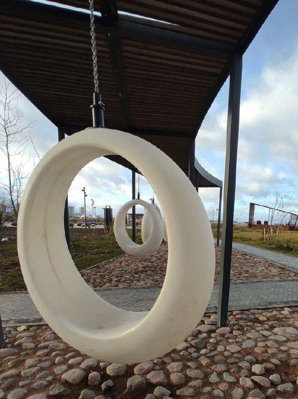 Крупный план круглой подвесной качели в форме кольца под навесом — дизайнерский элемент на набережной, создающий атмосферу уюта и деталей.