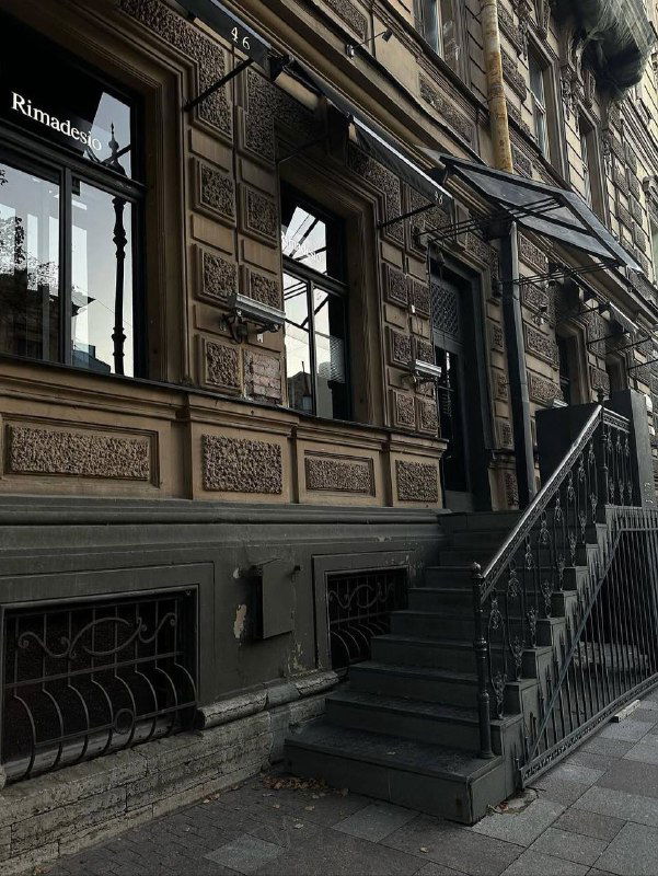 Ажурная каменная лестница у фасада дома рядом с витринами и декоративным цоколем — интересная точка для снимков с глубиной.