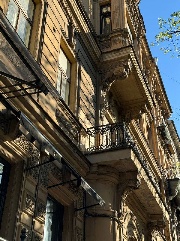 Ракурс на балкон и карнизы исторического здания: архитектурные детали, тёплая фактура фасада и утончённые орнаменты над окнами.