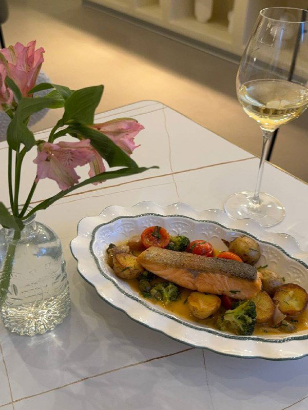 Стейк из лосося с молодым картофелем, брокколи и томатами, поданный на овальной тарелке — видно структуру филе и гарнир.