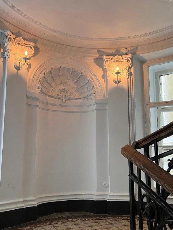 Интерьер парадной: ниша со лепниной и настенными светильниками рядом с декоративной лестницей в Особняке Слепцова в Петербурге.