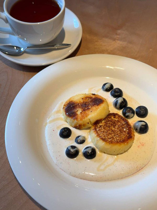 Тарелка сырников с ванильной сметаной и голубикой, сервировка на столе в минималистичном стиле в Salty.