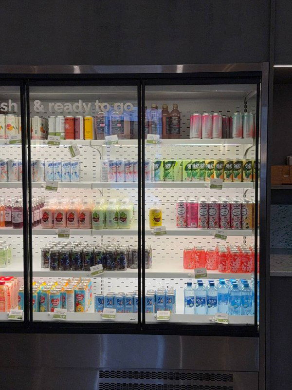 Холодильник с напитками в кафе: стеклянные дверцы, ассортимент банок и бутылок разных вкусов для удобного выбора.