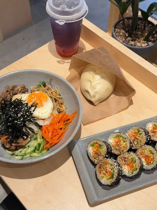 Набор блюд на столе: пибимпаб, роллы, Пегоди и напитки — вид сверху на порции, соусы и упаковку для выноса.