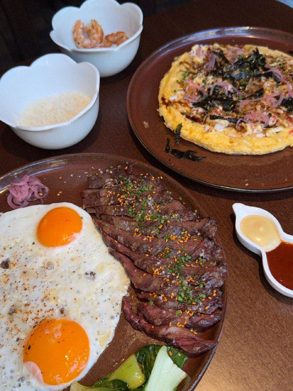 Стейк и яйца в бистро Ist: стриплойн и две глазуньи на тарелке, рядом соус и гарнир — плотный сытный завтрак в азиатском стиле.