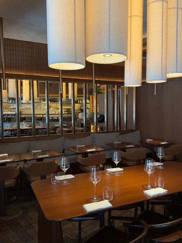 Длинный стол в бистро Ist: сервировка для гостей, бокалы, салфетки и каменная барная стойка на фоне зеркал и деревянного декора.