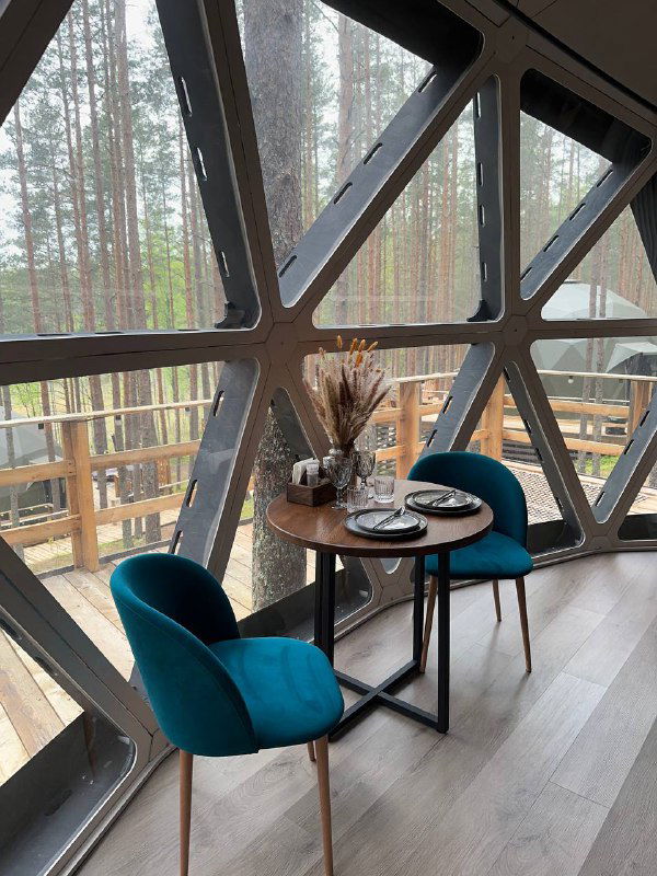 Интерьер купольной сферы: панорамное окно, небольшой столик и два кресла с видом на лес — уютная зона для завтрака и чтения в глэмпинге.