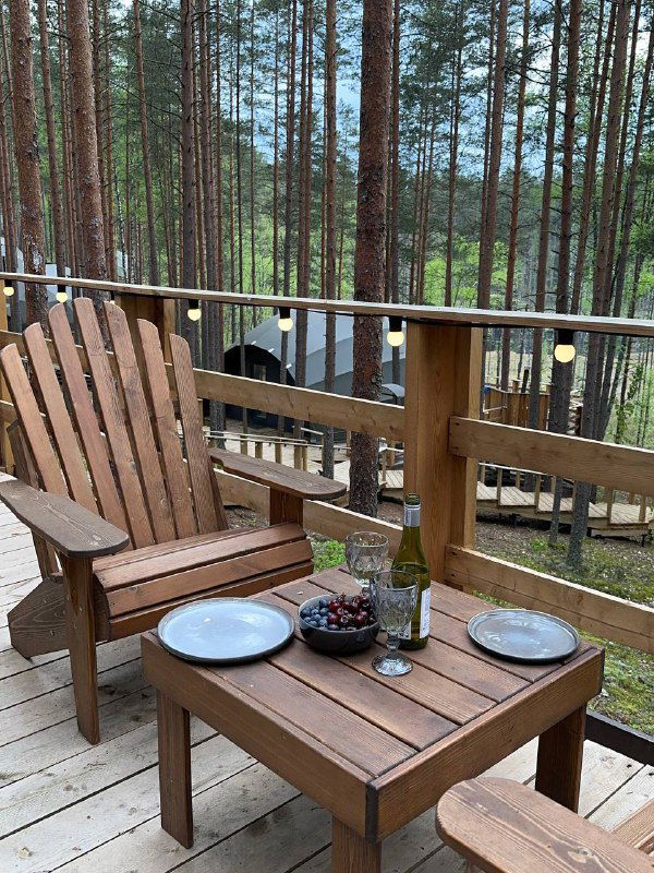 Деревянная терраса с набором столовой посуды и бокалом вина, два кресла и низкий столик — обеденная зона на открытом воздухе в Mystic Hills.