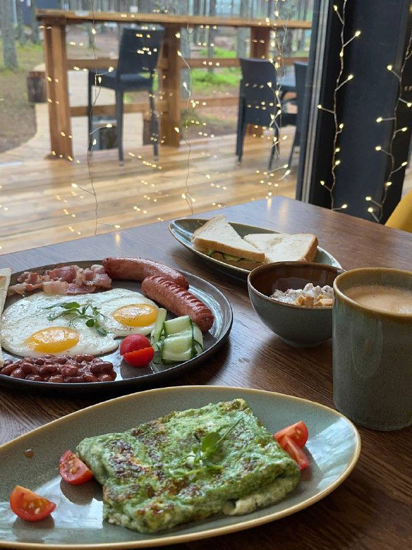 Завтрак в глэмпинге: глазунья, колбаски, плато с зеленью и напитки на столе у панорамного окна — пример утреннего меню Mystic Hills.