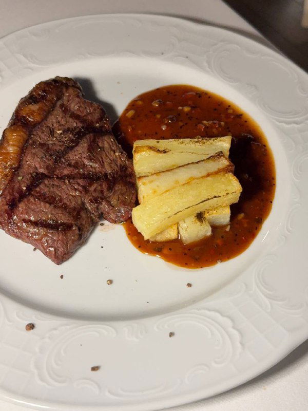 Крупный план стейка с перечным соусом и прямоугольными кусочками картофеля на белой тарелке — подача горячего блюда в «48 стульев».