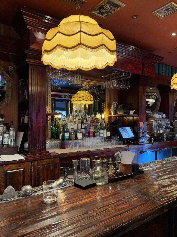 Барная стойка в ретро-стиле: деревянная поверхность, подвесные лампы в тканевых абажурах и стойка с бокалами и бутылками на фоне.