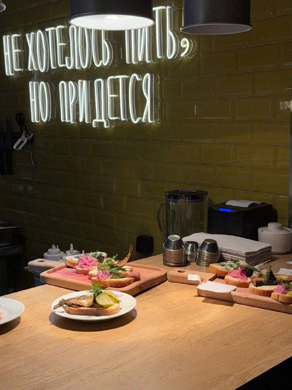 Стол с тарелками закусок и неоновая фраза на стене — зона подачи блюд в стиле домашней кухни 80-90-х с деревянной поверхностью.