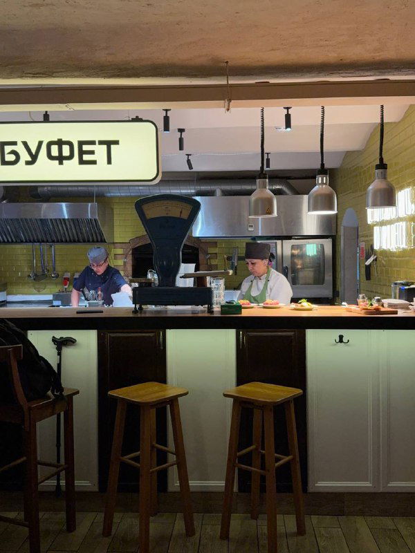 Буфет с поварами за прилавком: кухня в полуоткрытом формате, вывеска «БУФЕТ» и ретро-шкала на переднем плане.