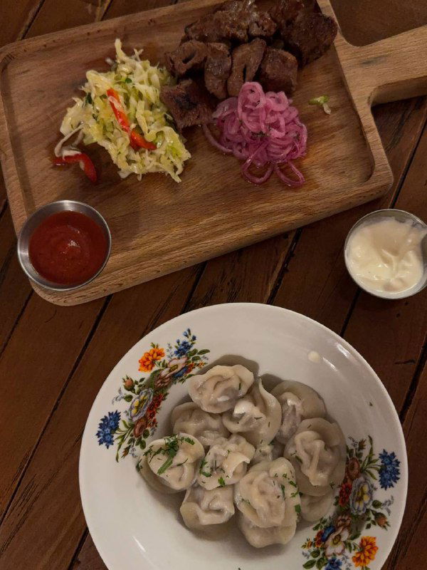 Пельмени на белой тарелке и кусочки шашлыка на деревянной доске с гарниром — иллюстрация основных блюд, указанных в заметке.