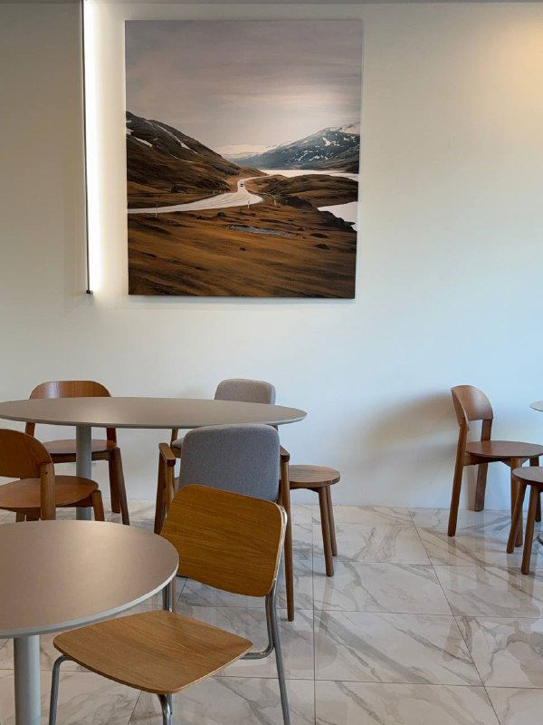 Пустой зал кофейни с небольшими столиками и фотографией пейзажа на стене — спокойная зона для завтрака.