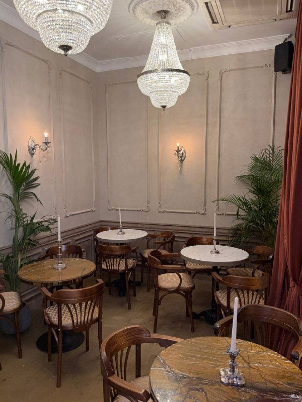 Пустой зал с хрустальными люстрами, круглыми столиками и деревянными стульями — воссозданная историческая атмосфера внутреннего зала бара.