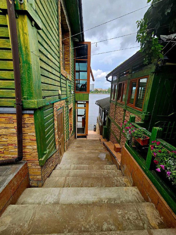 Широкий вид лестницы между зелёными домами: ступени ведут вниз к набережной, видны деревянные фасады и цветочные ящики.