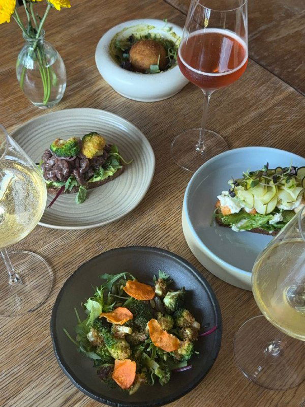 Несколько закусок и бокалы с вином на деревянном столе: брускетта, салат и текстура сервировки в авторском стиле.