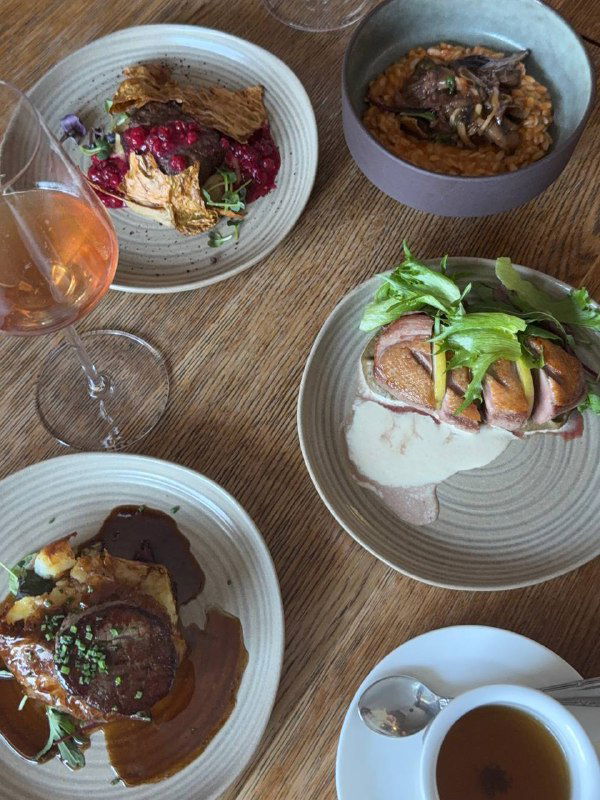 Стол с несколькими основными блюдами: утиная грудка, горшочек с рагу и аккуратная подача в нейтральной керамике.