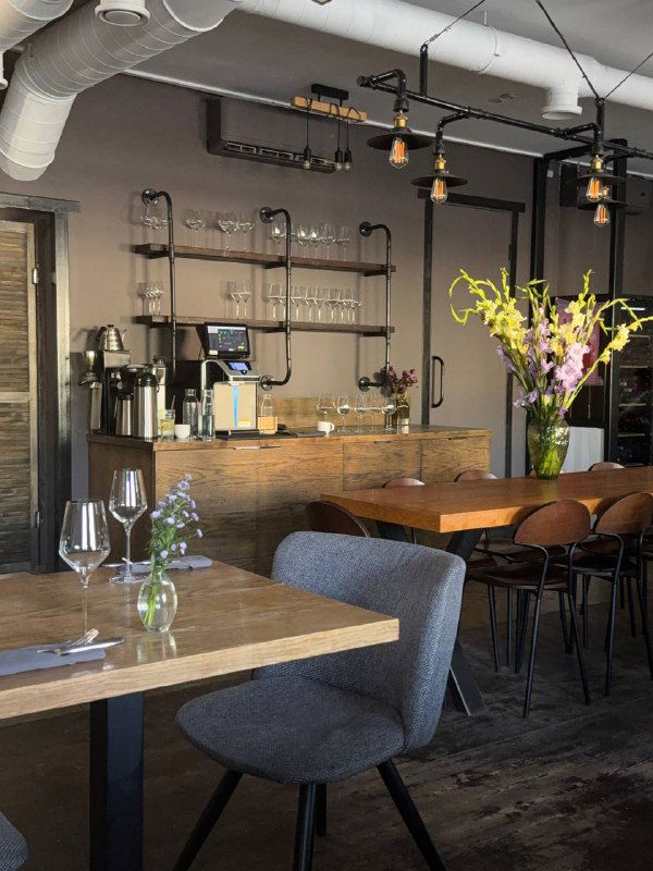 Уютный уголок кафе: столы, стулья, стойка с кофемашиной и минималистичный дизайн в индустриальном стиле.