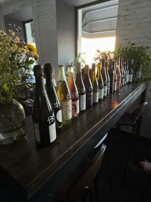 Ряд бутылок вина и сидячих мест на темной барной стойке — демонстрация большой винной карты кафе.