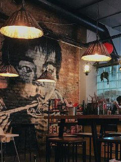 Кирпичная стена с большим муралом, над барной зоной висят декоративные лампы; интерьер сочетает индустриальные и азиатские мотивы.