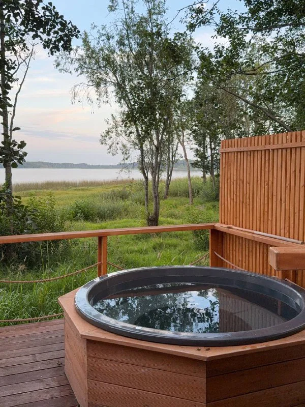 Купель на деревянной террасе домика Lembo с видом на прибрежные заросли и Лемболовское озеро — тихое место для расслабления на свежем воздухе.