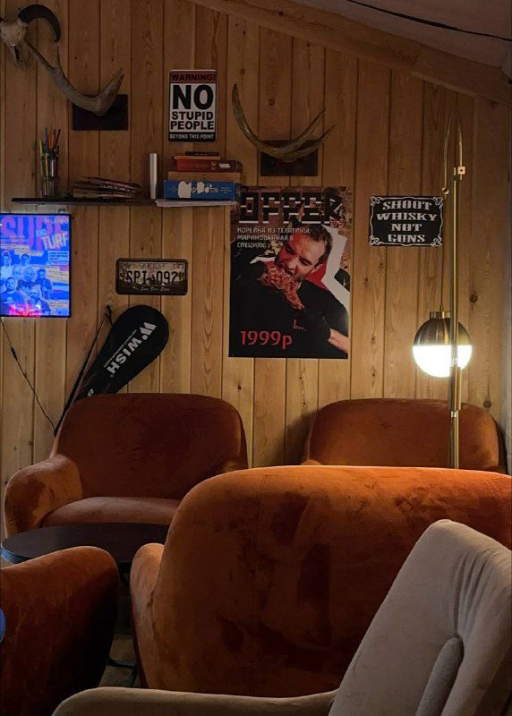 Уютная лаундж-зона внутри ресторана Chuck с бархатными креслами, ретро-постерами на деревянной стене и тёплой атмосферой для вечера кино и общения.