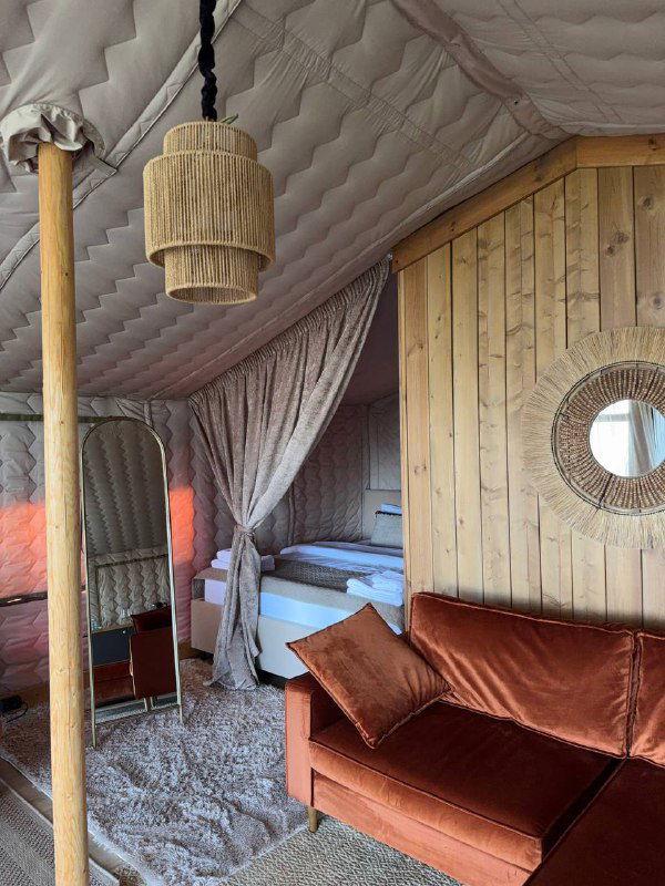 Внутреннее пространство домика Lembo: кровать с драпировками, диван и натуральные материалы в отделке, мягкое освещение создаёт глэмпинговую атмосферу.