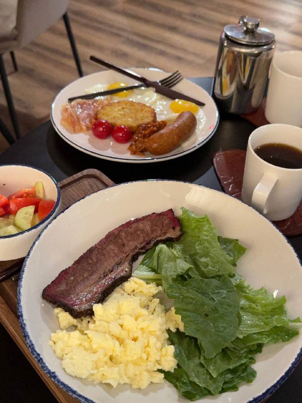 Завтрак в ресторане Chuck: тарелка со стейком, яичницей, зеленью и овощами, рядом чашка кофе и другие элементы утреннего сервиса, включённого в проживание.