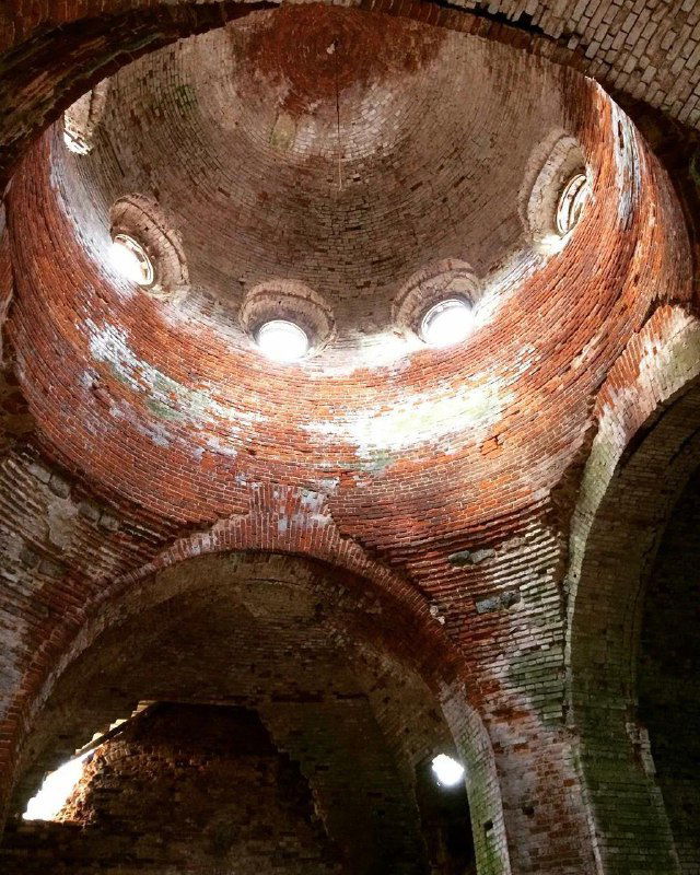 Вид изнутри купольного помещения разрушенной церкви в Хотнеже: кирпичная кладка с круглыми световыми отверстиями и эффектным распределением света и тени.