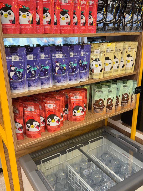 Полка с разнообразными фасованными продуктами и напитками в витрине KONO — ассортимент снеков и добавок рядом с кассой.