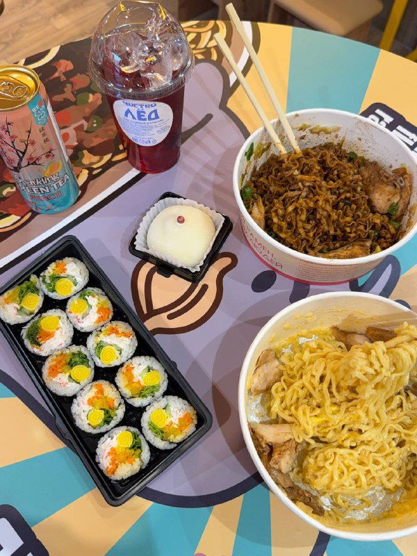 Вид сверху на стол: две тарелки рамена, роллы кимпаб, моти и напитки — композиция нашего заказа в KONO на Восстания.