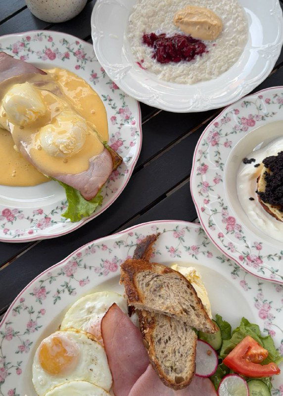 Тарелки со завтраком: яйца, соус и гарнир на фарфоровой посуде — утренний стол в одном из кафе региона, расселение блюд крупным планом.