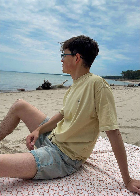 Человек в футболке сидит на песчаном пляже и смотрит на море — кадр с расслабленным отпускным настроением на берегу Балтийского моря.